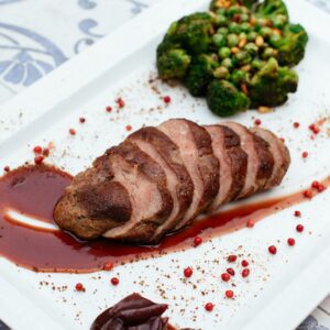 Deliciously plated duck breast with broccoli and sauce on a white plate.