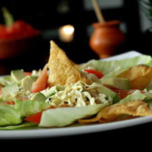 Delicious Mexican salad featuring avocado, lettuce, tomato, and crispy chips on a plate.