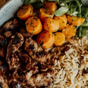 Delicious grilled meat with carrots, rice, and greens, perfect for healthy meals.
